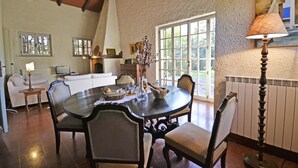 A dining area with a round table, chairs, and a lamp. There is a fireplace and a window with a view of greenery. - Villa in Il Passaggio with 5 bedrooms sleeps 10 (Il Passaggio)