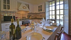 A dining area with a table set for a meal, kitchen cabinets, a stove, and a view through a large window. - Villa in Il Passaggio with 5 bedrooms sleeps 10 (Il Passaggio)