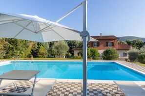 Ein Swimmingpool mit einem weißen Sonnenschirm, Liegestühlen und einem Haus im Hintergrund.