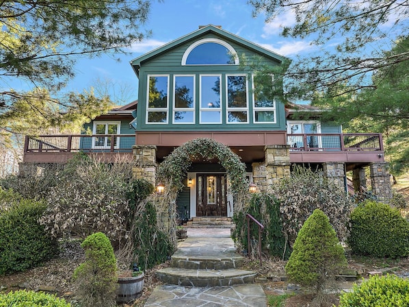 A two-story house with a stone facade, a large arched entrance, and a balcony with a railing.