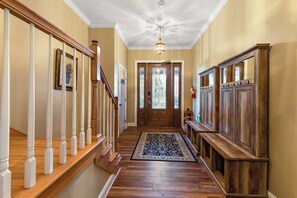 A hallway with wooden flooring, a staircase with white balusters, a patterned rug, and a wooden bench.