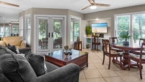 A spacious living room with a large sofa, a dining table with chairs, a ceiling fan, and a TV mounted on the wall. - Ground Floor, Screened Porch, Free Beach Chair Service, Large Pool (Miramar Beach)