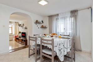 Un comedor con una mesa dispuesta para cuatro personas, sillas, un televisor y una cocina a la vista.