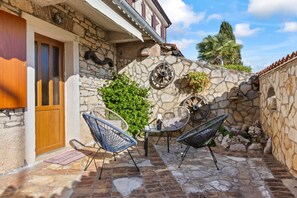 Edificio de piedra con puerta de madera, paredes de piedra y un pequeño patio con sillas de mimbre y una mesa.