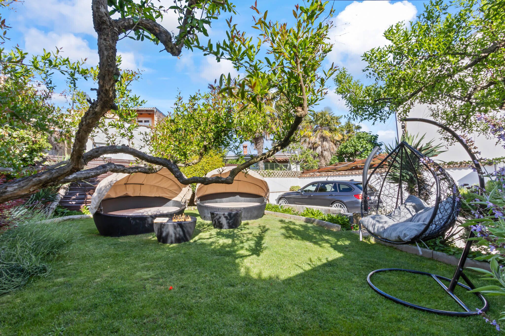 A garden with outdoor seating, a swing chair, and a car parked nearby.