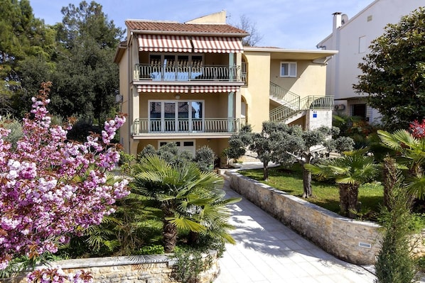 A multi-story building with balconies, a stone pathway, and lush greenery.