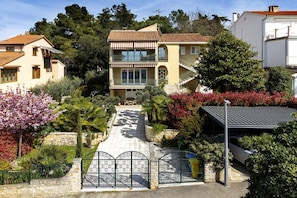 A two-story house with a balcony, surrounded by lush greenery and flowering plants.