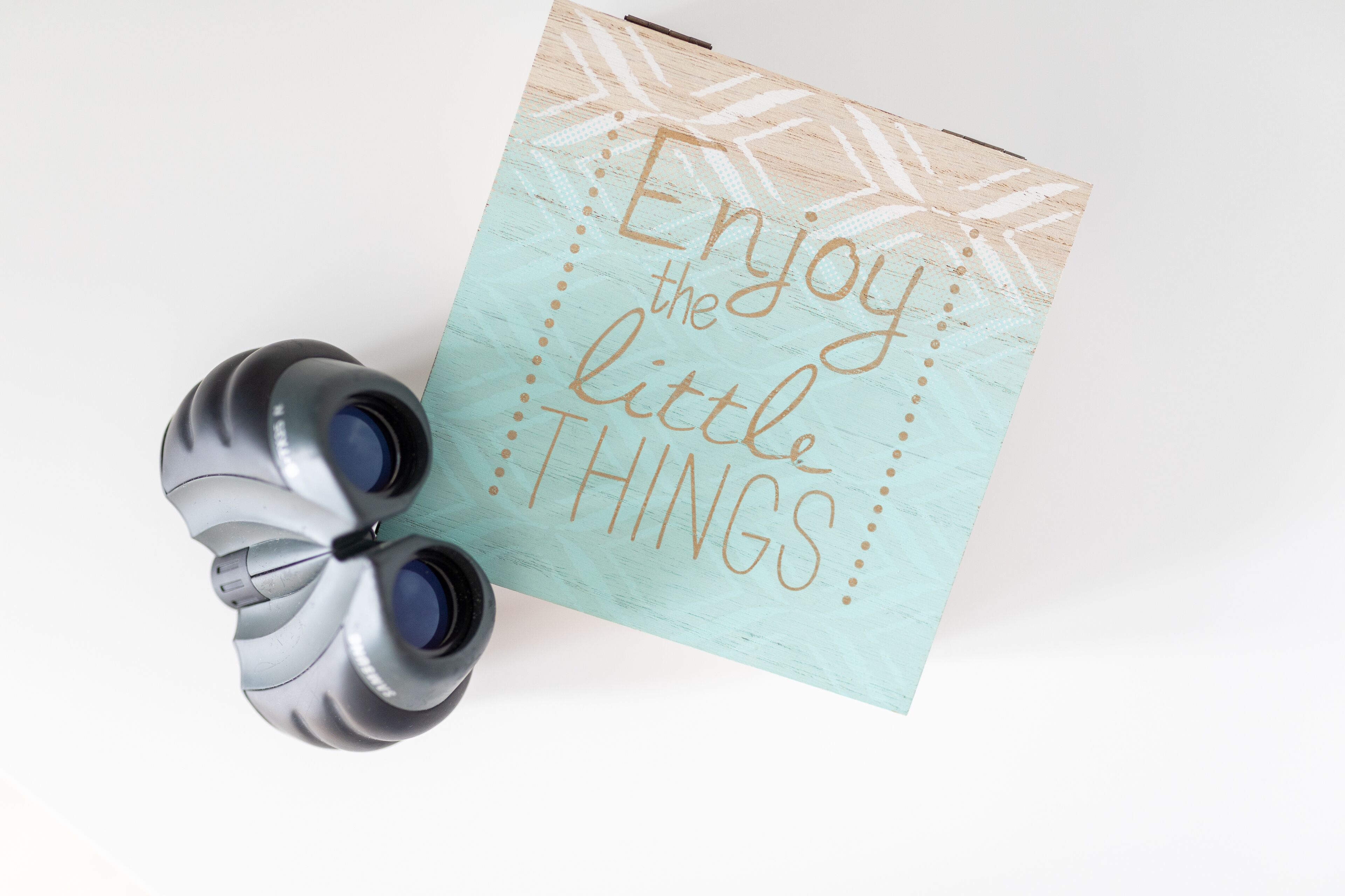 A handwritten note with the text "Enjoy the little things" alongside a pair of binoculars.