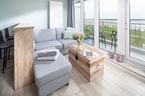 A modern living room with a grey sofa, a wooden coffee table, and a view of the sea through large windows. - Top sea view, one-room apartment Kaiserhof 312, modern, directly on the beach (Norderney)