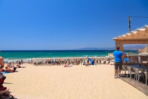 A beach with a wooden deck, umbrellas, and beach chairs.
