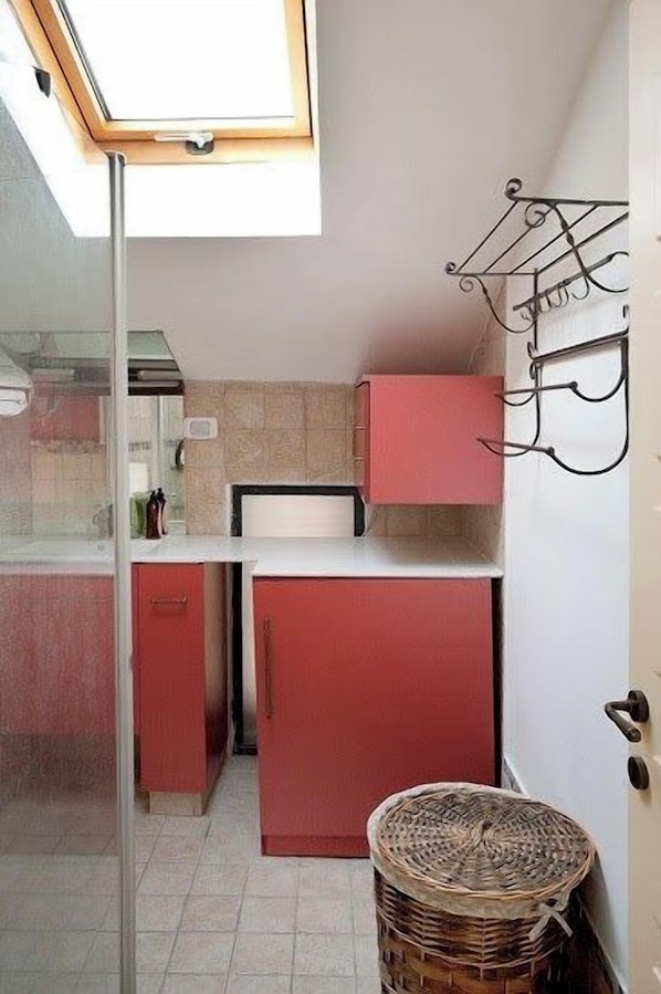 A compact kitchen with a skylight, a red refrigerator, and a wicker basket.