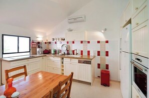 A compact kitchen with white cabinetry, a wooden dining table, and a red trash bin.