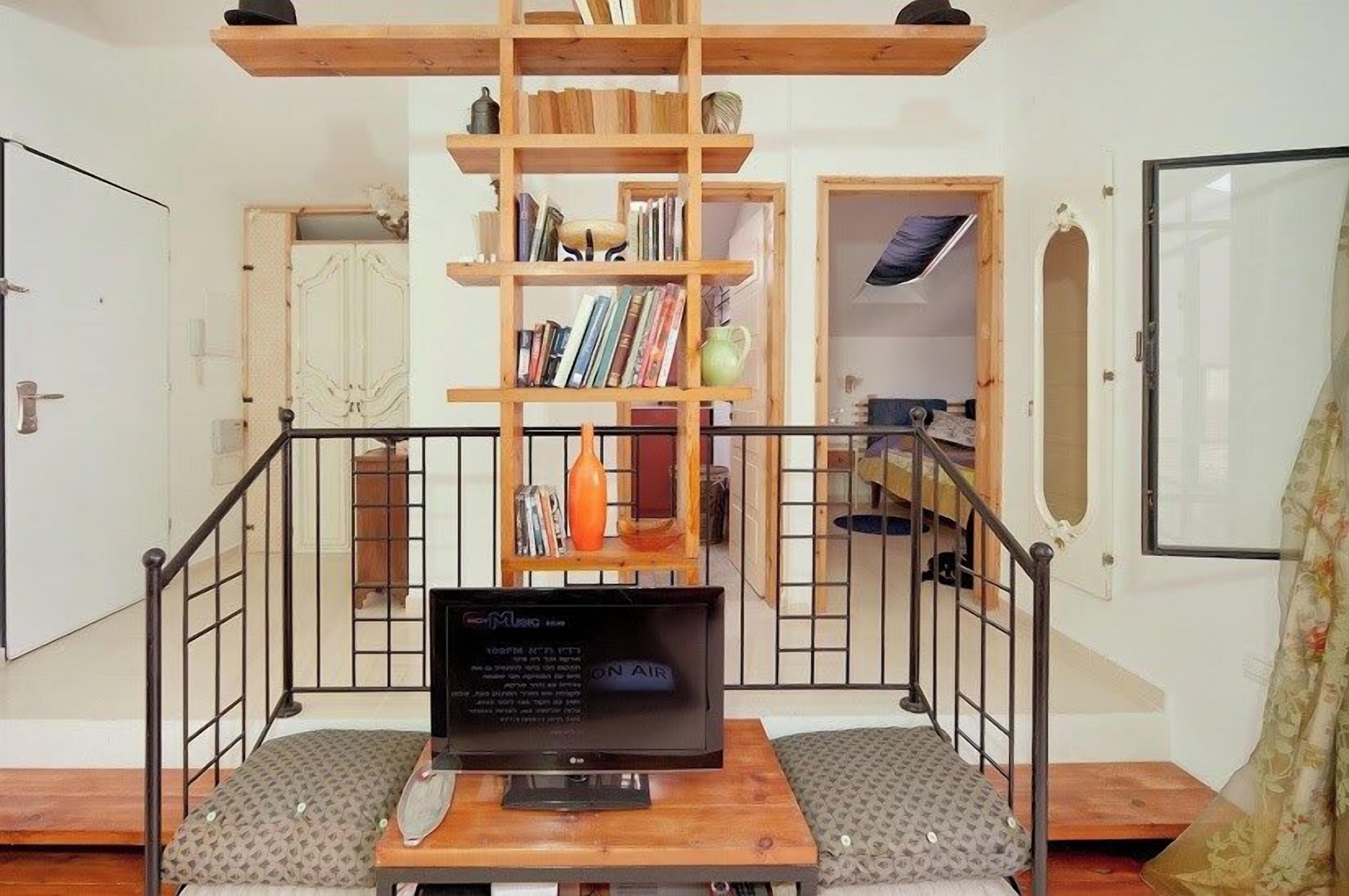 A room with a bed, a wooden ladder, a bookshelf, and a desk with a computer monitor.