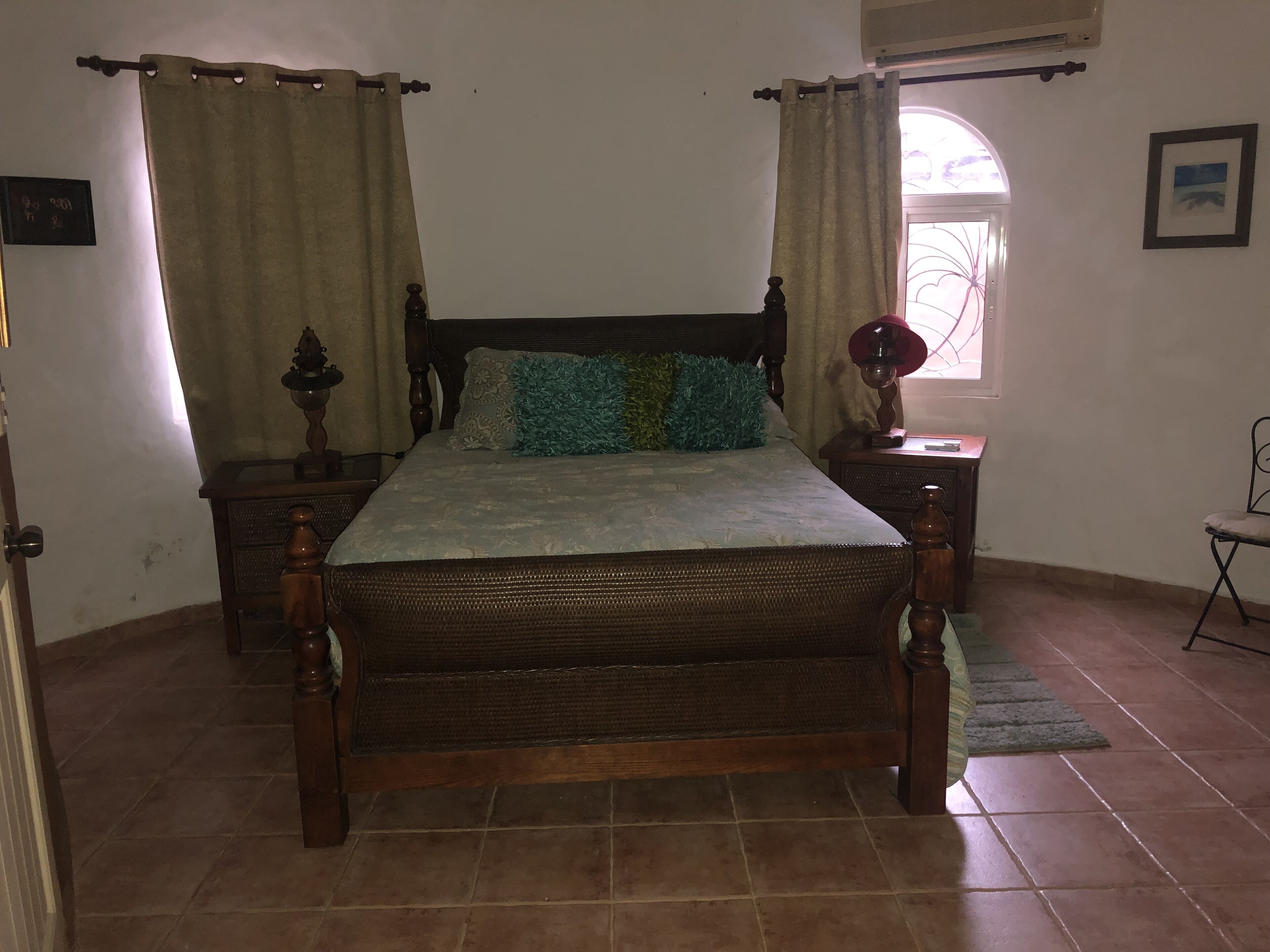 A bedroom with a wooden bed, two nightstands, a window with curtains, and a door.