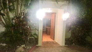 An entrance with a stone pathway leading to a wooden door, surrounded by lush greenery and palm trees. - Villa Vista Mar (Sosúa)