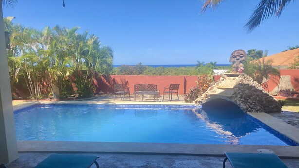 A swimming pool with two lounge chairs, a stone wall, and a view of the ocean. - Villa Vista Mar (Sosúa)