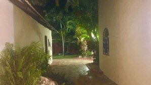 A narrow pathway flanked by white walls and tropical plants, leading to a shaded area with a palm tree. - Villa Vista Mar (Sosúa)