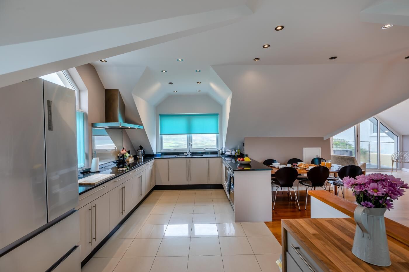 Una cocina moderna con una isla central, un comedor con mesa de madera y vistas al exterior a través de amplios ventanales.