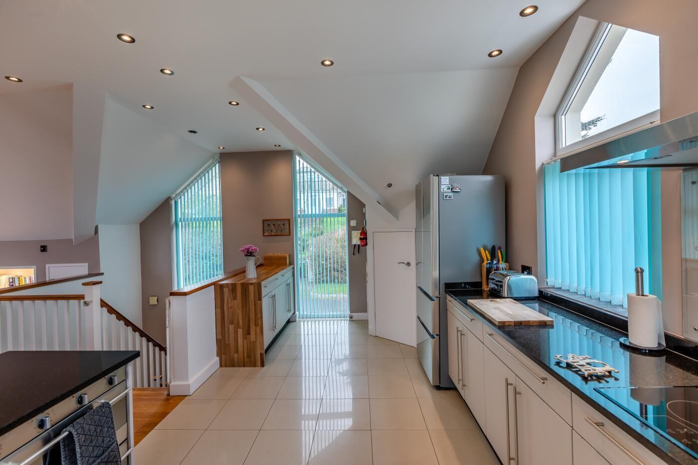 A modern kitchen with a central island, a refrigerator, and a window with blinds.