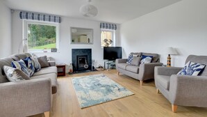 A living room with two sofas, a fireplace, a TV, and a lamp. - 4 Bed in Ilfracombe (oc-autumn) (Ilfracombe)