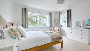 A bedroom with a wooden bed, white bedside tables, a dresser, and a window with curtains. - 4 Bed in Ilfracombe (oc-autumn) (Ilfracombe)