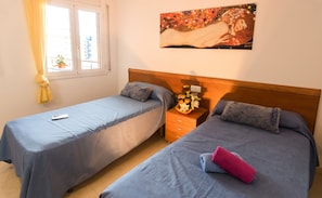 A hotel room with two single beds, a wooden headboard, a nightstand with a vase of flowers, and a painting on the wall.
