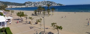 A beach with a volleyball net, palm trees, and a clear view of the sea and a hill in the background.