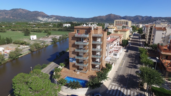 A multi-story building with balconies, a swimming pool, and a river in the background.