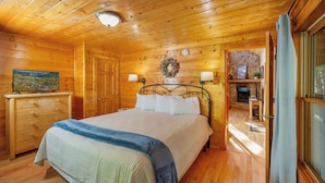 A wooden-paneled room with a bed, a television on a dresser, and a fireplace.
