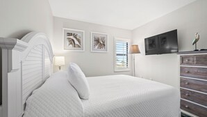 Een slaapkamer met een bed, een dressoir, een televisie en twee kunstwerken aan de muur.