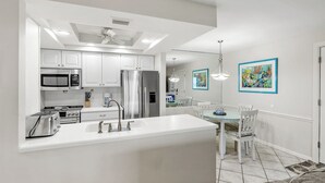 Een moderne keuken met witte kasten, een centraal eiland en een eethoek met een glazen tafel en witte stoelen.