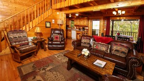 A cozy cabin interior with a wooden staircase, leather furniture, a dining area, and a kitchen. - Beautiful Mtn Views! Close to Dollywood & Attractions - Pool, Putt Putt, Tennis (Sevierville)
