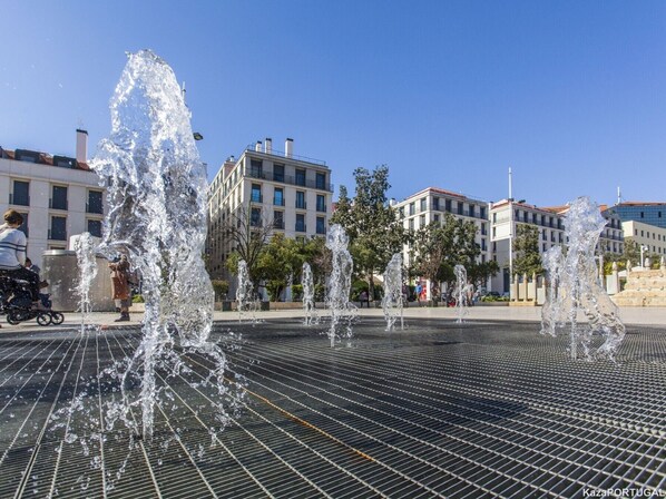 Une place publique agrémentée d’une fontaine et bordée de bâtiments modernes.
