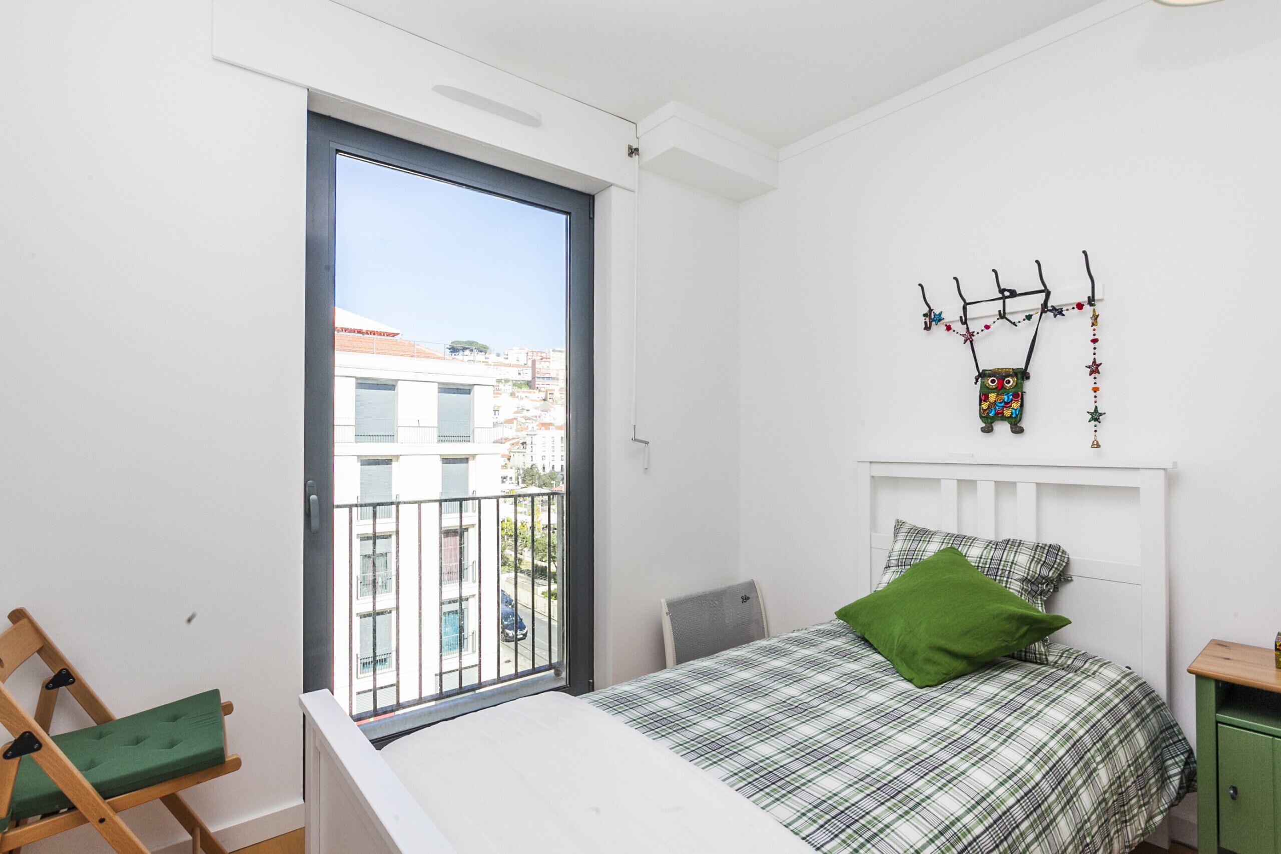 Un dormitorio con cama, una silla verde, un balcón y un adorno en la pared.