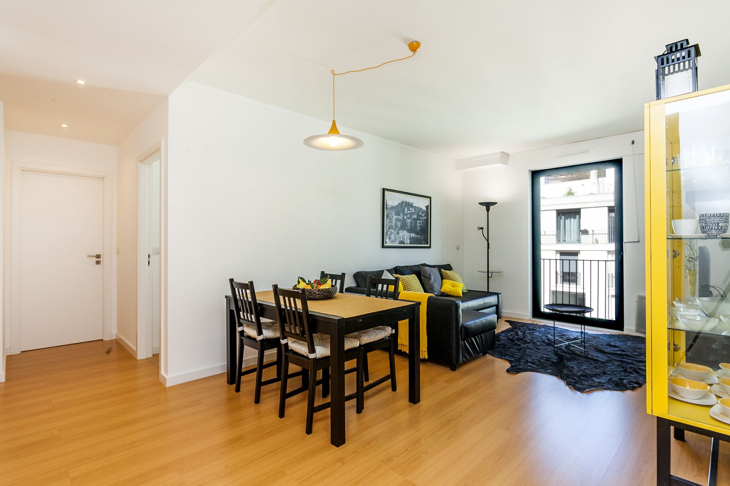 A modern living room with a dining area, a sofa, a black leather rug, and a yellow cabinet.