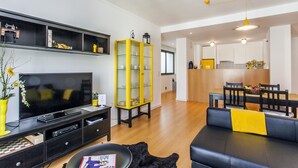 Un soggiorno moderno con una TV a schermo piatto, un mobiletto giallo, un divano in pelle nera e un'area pranzo con mobili in legno.