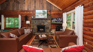 A log cabin interior with a stone fireplace, leather sofas, a pool table, and large windows. - Very Private w/ Beautiful Scenery of Creeks! Pool, Putt Putt, Fishing, Hiking (Sevierville)