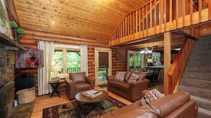 A log cabin interior with a wooden ceiling, a living room with leather sofas, a fireplace, and a staircase. - Very Private w/ Beautiful Scenery of Creeks! Pool, Putt Putt, Fishing, Hiking (Sevierville)