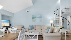 A living room with a television, two sofas, a coffee table, and a staircase.