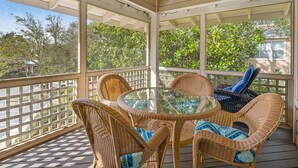 A covered outdoor seating area with wicker furniture and a glass table, overlooking a residential area.