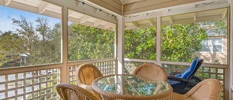 A covered outdoor seating area with wicker chairs and a glass table, overlooking a residential area.