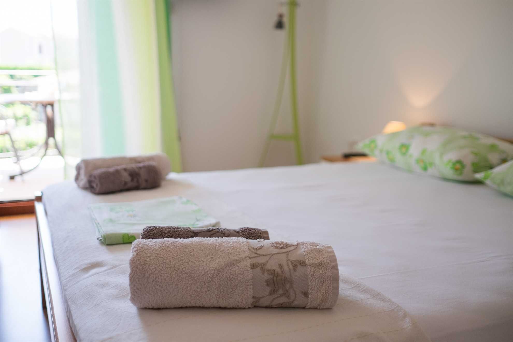 Cama bem arrumada com toalhas enroladas e um travesseiro verde.