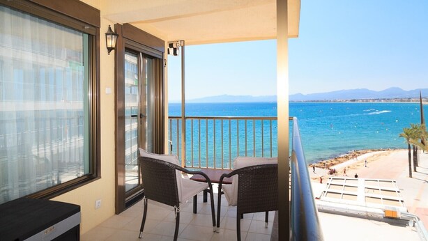 A balcony with a view of the sea, a table, two chairs, and a sofa.