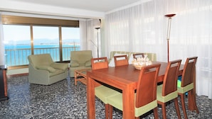 A hotel room with a dining table, chairs, a sofa, and a view of the sea.
