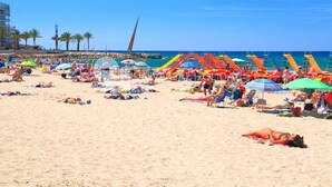 A beach with people sunbathing, colorful umbrellas, and a water slide.