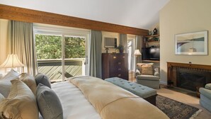 A hotel room with a large bed, a sofa, a television, a fireplace, and a view of the outdoors.