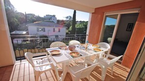 A balcony with a table set for two, white chairs, and a view of a residential area with houses and trees.