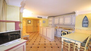 A compact kitchen with a tiled floor, a dining table with chairs, and a small island with a sink.