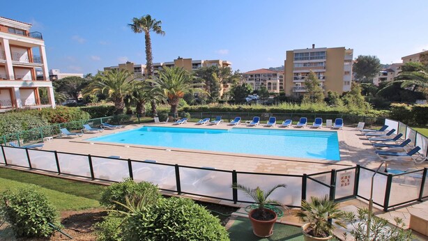 A swimming pool with lounge chairs, surrounded by greenery and buildings.