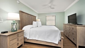 Une chambre à coucher comprenant un lit, des tables de chevet, une commode, un téléviseur et un ventilateur de plafond.